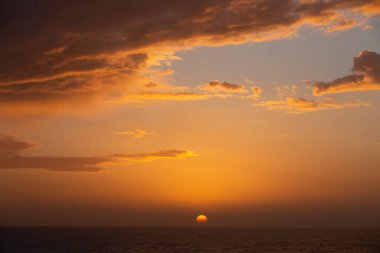 Denizin üzerinde gün batımı, bulutlar güzel havada.