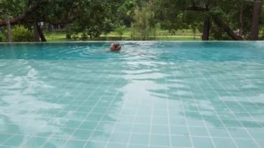 Beautiful long-haired woman swims in an outdoor infinity pool against the backdrop of tropical vegetation, 10 bit prores high quality 4k footage