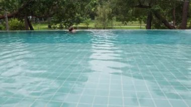 Beautiful long-haired woman swims in an outdoor infinity pool against the backdrop of tropical vegetation, 10 bit prores high quality 4k footage