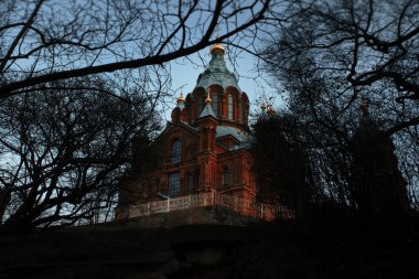Ağaçların arasından geçen eski kırmızı tuğladan yapılmış bir kilise. Kiliseye ve ağaçlara odaklanmış bir kilise.