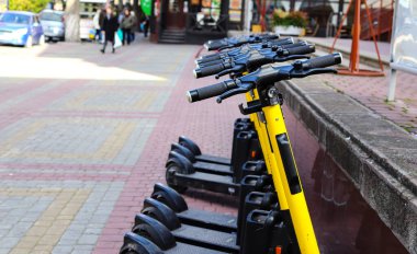 Şehir sokaklarında modern elektrikli scooterların park yeri. Modern siyah ve sarı elektrikli scooterlar modern bir şehrin caddesinde park edilmiş.