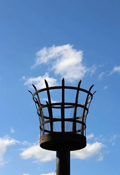 白い雲と青い空の背景を持つ極にワイヤーメッシュインサート付きの金属バスケット火災ビーコン ロイヤリティフリーのストック画像