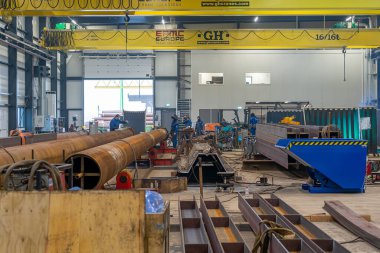 Mobil vinçleri, çelik yığınları ve kirişleri olan ve kaynakçıların çalıştığı bir çelik fabrikasının içi..