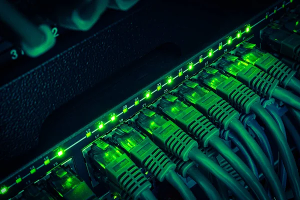 Close up of green network cables from data center connected with green patch cords to black switch glowing in the dark