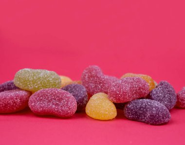 Pembe arkaplan çerçeveli ekşi jöleli şeker yığını. Metin için kopyalama alanı olan pembe bir arkaplanda izole edilmiş ekşi tatlılar