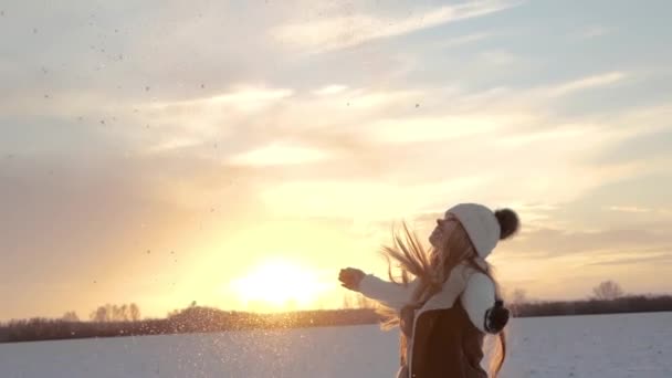 Зимой девушка на закате бросает снег в воздух. Медленное движение в золотой час — стоковое видео