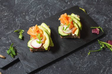 Koyu çavdar ekmeği, avokado, tütsülenmiş somon ve turp, siyah arkaplan..