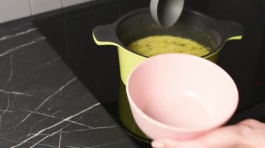Genç kadın evde öğle yemeği için tencereye sıcak çorba dolduruyor.