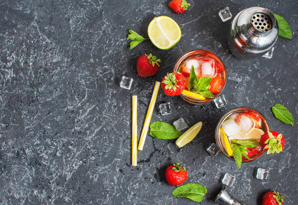 Summer refreshing mojito cocktail with strawberry, mint and lime with shaker for whipping drinks on a dark stone table. Top view and copyspace