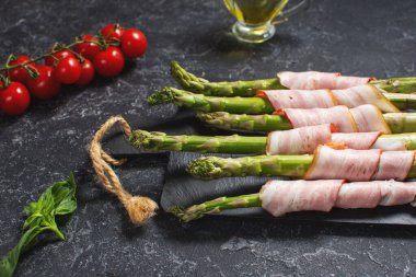 Taze yeşil kuşkonmaz, siyah taş bir masada pastırmaya sarılmış.