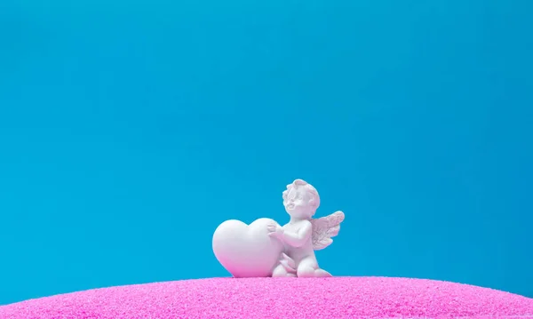 Pembe kum ve mavi arka planda kalbi olan bir melek. Minimum arka plan konsepti. Havada aşk kokusu var..