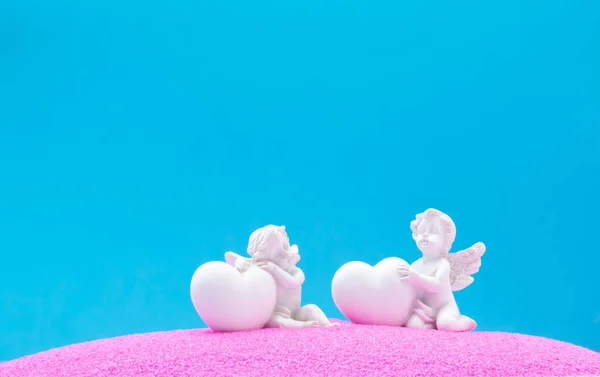 Pembe kum ve mavi arka planda kalpleri olan melekler. Minimum arka plan konsepti. Havada aşk kokusu var..
