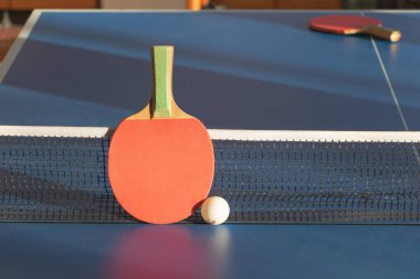 Kırmızı bir pinpon raketi ve mavi bir pinpon masasında beyaz bir top..