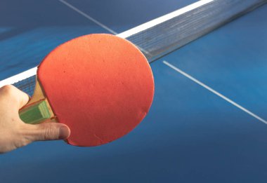 Mavi bir tenis masasının üzerinde elinde kırmızı bir pinpon raketi..