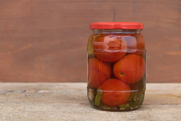 Beberapa tomat yang direndam dalam guci tertutup dengan latar belakang kayu — Stok Foto