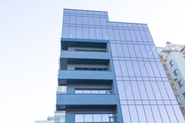 Beyaz gökyüzünde camdan pencereleri olan bir bina..