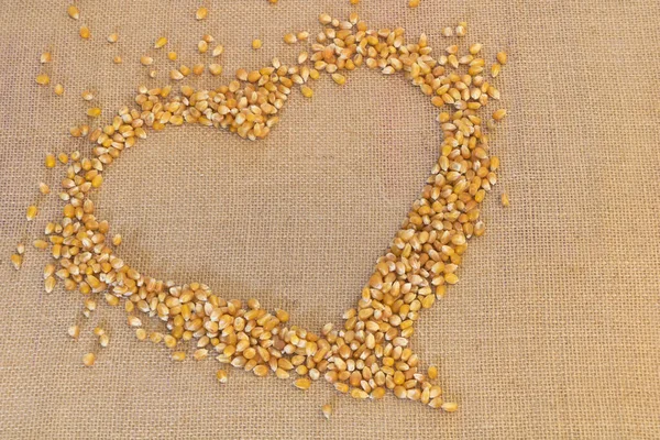 Granos de palomitas crudas en forma de corazón sobre fondo hessiano — Foto de Stock