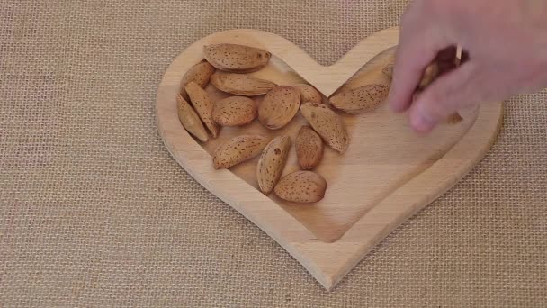 Een Man Vult Een Hartvormige Houten Plaat Met Amandelen — Stockvideo