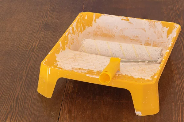 Yellow painters tray and roller with dried white paint on hardwood floor.