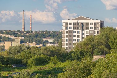 Güzel bir yaz gününde, yüksek katlı apartman binası. Uzakta endüstriyel bacalar var..