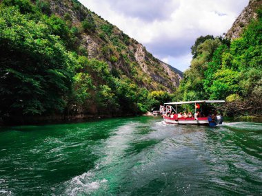 Dağların arasında turistlerle dolu bir tekne ve Matka Kanyonu 'nda zümrüt renkli su yüzüyor. Kavram: suda yürüyüş, Makedonya 'da tatil.