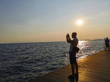 Deniz kenarındaki setin kenarında oturan genç, atletik bir adamın portresi. Gün batımını ve doğayı sever. Seyahat, tatil, Yunanistan