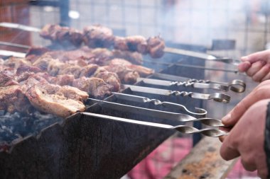 Bir adam ateşte et pişirir. Eller ve barbekü yakın çekim. Domuz budu ızgara. Kızarmış havuç. Yağlı yiyecekler, BDT ülkelerinin şenlikli yemekleri. 1 Mayıs, çalışma günü. Vejetaryen olmayan yemekler. Sokak yemeği.