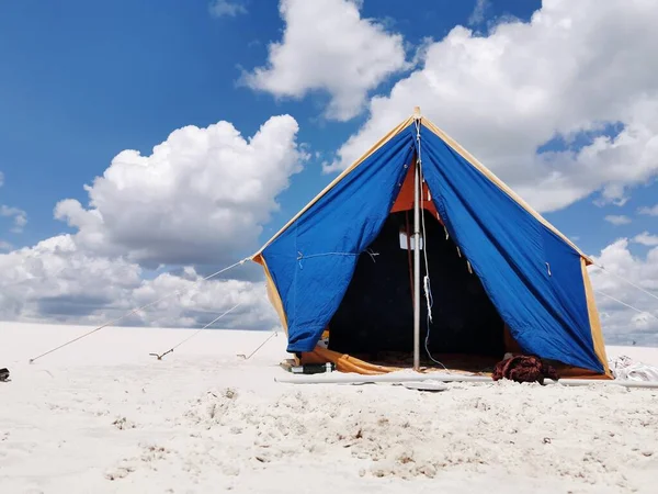 A tourist tent stands on the white sand on the beach. Summer tent for family outdoor recreation. camping, summer.Blue-yellow fabric. Active rest, family leisure away from civilization
