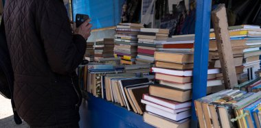 Bit pazarındaki bir adam almak için kitap seçer. Eski kitapların geniş bir yelpazesi açık pazarda. Ev kütüphanesinin açık hava satışı. Dergi ve ansiklopedi dağıtımı