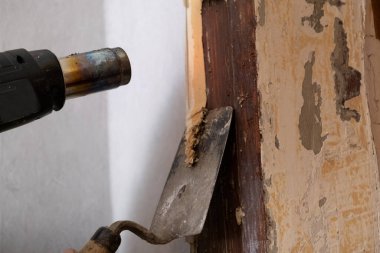 Apparatus for removing old paint. Building hair dryer in the process. Repair work inside the house. Removal of the old layer painted with a spatula