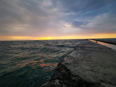 Odessa sahilinden (Ukrayna) Karadeniz manzarası. Sakin bir deniz, bir martı dalgakıranın üzerinde oturur. Suyun üstünde şafak sökerken. Turistik bölge, dinlenme alanı.