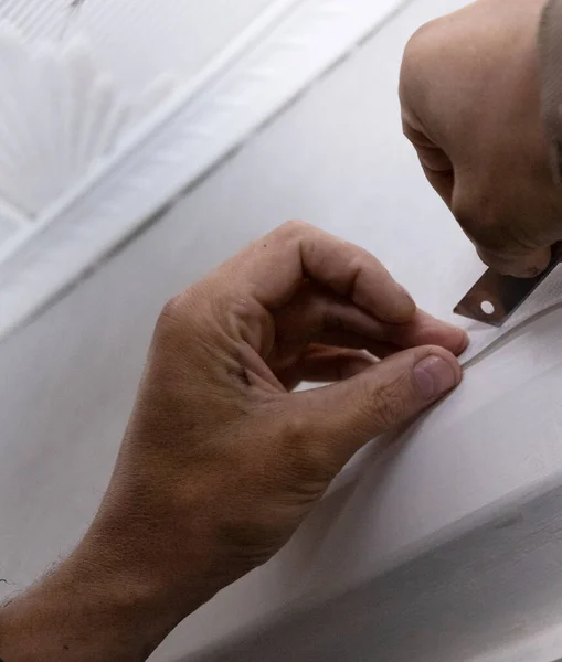 Close-up of male hands. The painter cuts off the excess of fleisin wallpaper with a sharp blade, the repair process. Stationery knife at work.