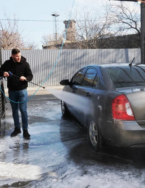 Street car wash self-service.Washing in the open air.A man washes a vehicle with shampoo under strong water pressure. Property maintenance, dry cleaning