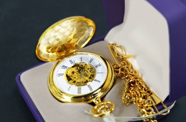 Koyu mavi arka planda pahalı bir beyefendinin cep saati. Eski tarz bir altın cep saati yanında zincir olan mor bir kutuda yatıyor. Boşluk afişini kopyala.