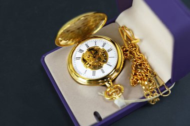 Koyu mavi arka planda pahalı bir beyefendinin cep saati. Eski tarz bir altın cep saati yanında zincir olan mor bir kutuda yatıyor. Boşluk afişini kopyala.