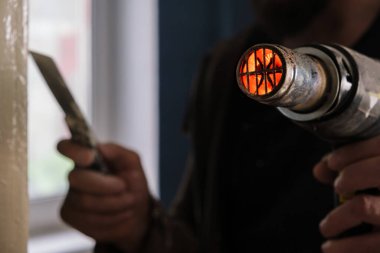 Eski boyaları çıkarmak için bir cihaz. Saç kurutma makinesi yapılıyor. Evin içinde tamirat var. Eski boyalı katmanı bir spatulayla kaldırıyorum.