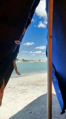 Sahildeki beyaz kumun üzerinde bir turist çadırı duruyor. Aile gezisi için yaz çadırı. Kamp, yaz. Mavi-sarı kumaş. Aktif dinlenme, aile uygarlıktan uzakta vakit geçirme.