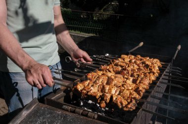 Bir adam ateşte et pişirir. Elleri yakın çekim ve şiş kebap. Izgarada domuz boynu pişirmek. Kızarmış havuç. Yağlı yiyecekler, BDT ülkelerinin şenlikli yemekleri. 1 Mayıs, İşçi Bayramı. Vejetaryen yemeği değil.