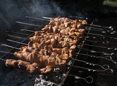 Büyük et parçaları ızgarada kömürde kızartılır. Kömürden duman, karanlık arka plan, dizilmiş şiş kebap. Yağlı, lezzetli yemekler. Ormanda piknik yapmak için büyük bir şirket için yiyecek.