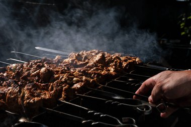 Bir adam ateşte et pişirir. Elleri yakın çekim ve şiş kebap. Izgarada domuz boynu pişirmek. Kızarmış havuç. Yağlı yiyecekler, BDT ülkelerinin şenlikli yemekleri. 1 Mayıs, İşçi Bayramı. Vejetaryen yemeği değil.