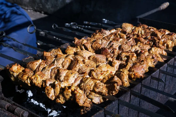 Large pieces of pork meat are fried on coals in the grill. Smoke from coal, dark background.Skewers with strung shish kebab. Fatty delicious food. Food for a large company for a picnic in the forest