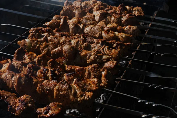 Large pieces of pork meat are fried on coals in the grill. Smoke from coal, dark background.Skewers with strung shish kebab. Fatty delicious food. Food for a large company for a picnic in the forest