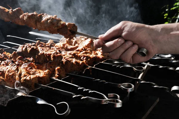 Bir adam ateşte et pişirir. Elleri yakın çekim ve şiş kebap. Izgarada domuz boynu pişirmek. Kızarmış havuç. Yağlı yiyecekler, BDT ülkelerinin şenlikli yemekleri. 1 Mayıs, İşçi Bayramı. Vejetaryen yemeği değil.
