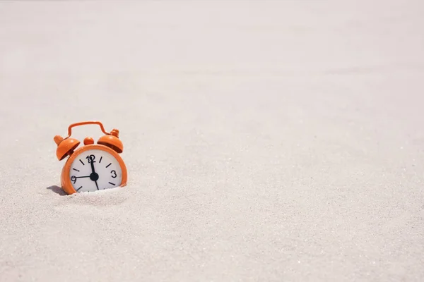 Orange alarm clock on white quartz sand. Concept: vacation time, tourist season by the water, beach time. copy space, summer banner.