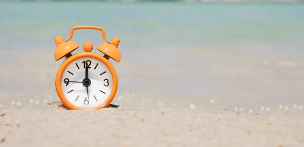 Orange alarm clock on the beach, sand and azure water. Concept: vacation time, tourist season by the water, beach time. copy space, summer banner.