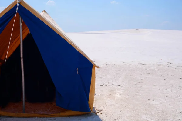 A tourist tent stands on the white sand on the beach. Summer tent for family outdoor recreation. camping, summer. Blue-yellow fabric. Active rest, family leisure away from civilization