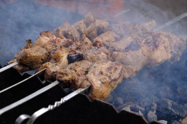 Bir adam ateşte et pişirir. Elleri yakın çekim ve şiş kebap. Izgarada domuz boynu pişirmek. Kızarmış havuç. Yağlı yiyecekler, BDT ülkelerinin şenlikli yemekleri. 1 Mayıs, İşçi Bayramı. Vejetaryen yemeği değil.