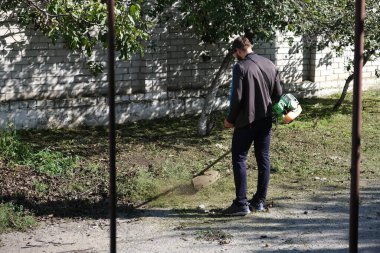 Çim biçme makinesi. Bir adam kalın bir çim biçer. Bahçe bakımı, manzara iyileştirmesi. Bahçe malzemeleri. Elektrikli çim biçme makinesi. Bitki ve yabani otların temizlenmesi. yatay resim