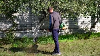 Çim biçme makinesi. Bir adam kalın bir çim biçer. Bahçe bakımı, manzara iyileştirmesi. Bahçe malzemeleri. Elektrikli çim biçme makinesi. Bitki ve yabani otların temizlenmesi. yatay resim