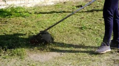 Çim biçme makinesi. Bir adam kalın bir çim biçer. Bahçe bakımı, manzara iyileştirmesi. Bahçe malzemeleri. Elektrikli çim biçme makinesi. Bitki ve yabani otların temizlenmesi. yatay resim